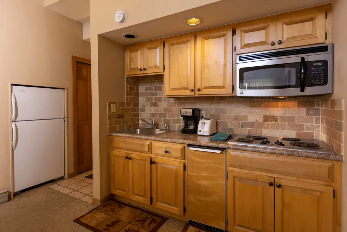 A cozy, well-lit kitchen featuring wooden cabinetry, a tiled backsplash, and a full suite of modern appliances including a microwave, toaster, coffee maker, and compact dishwasher. The inviting atmosphere suggests both efficiency and comfort for meal preparation and cleanup, and the layout is practical for social cooking or casual snacks.
